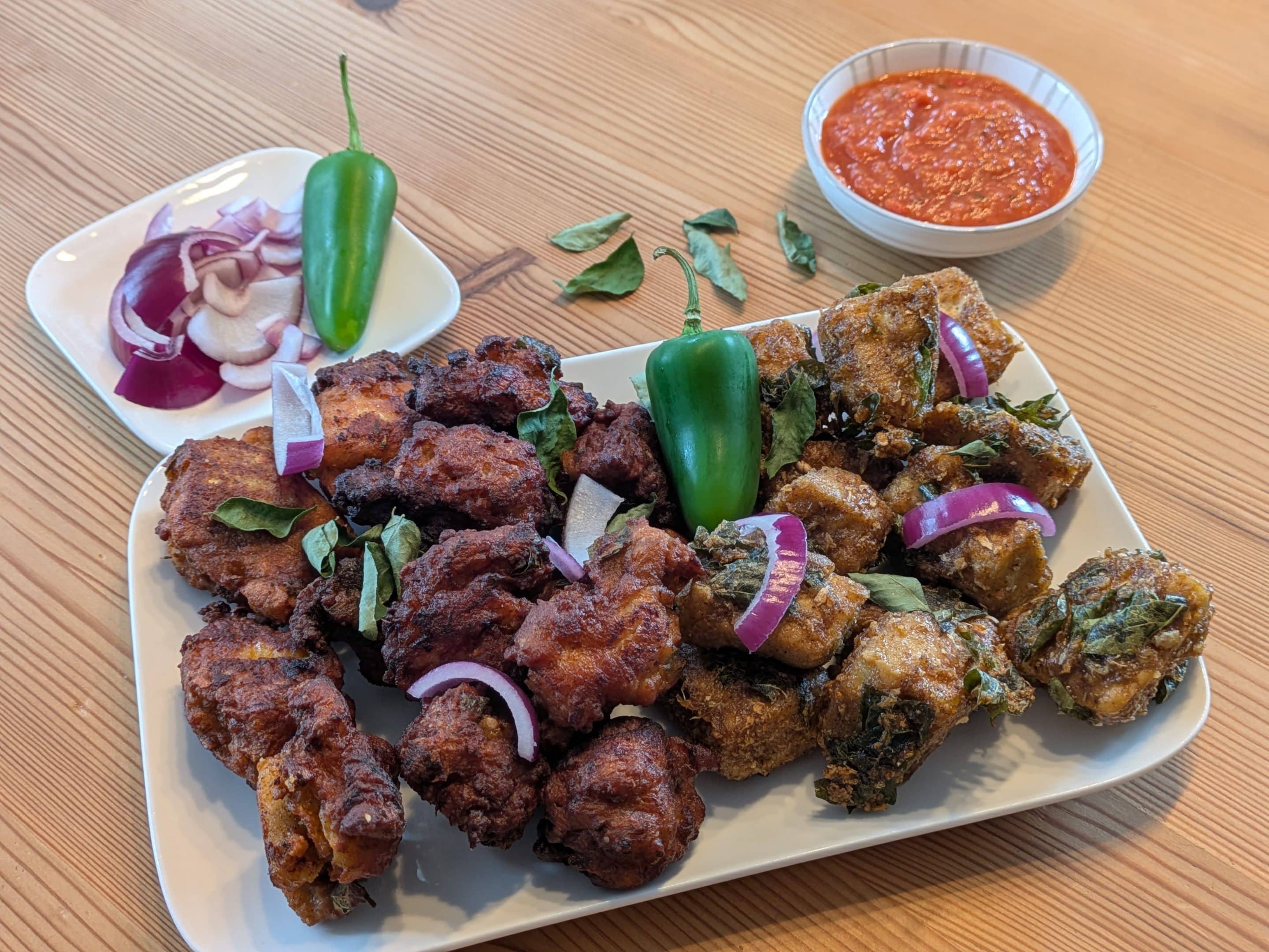 Fertiges Chicken 65 mit Hähnchen und Tofu, angerichtet mit roten Zwiebeln, grüner Chili und Dip Fertiges Chicken 65 mit Hähnchen und Tofu, angerichtet mit roten Zwiebeln, grüner Chili und Dip